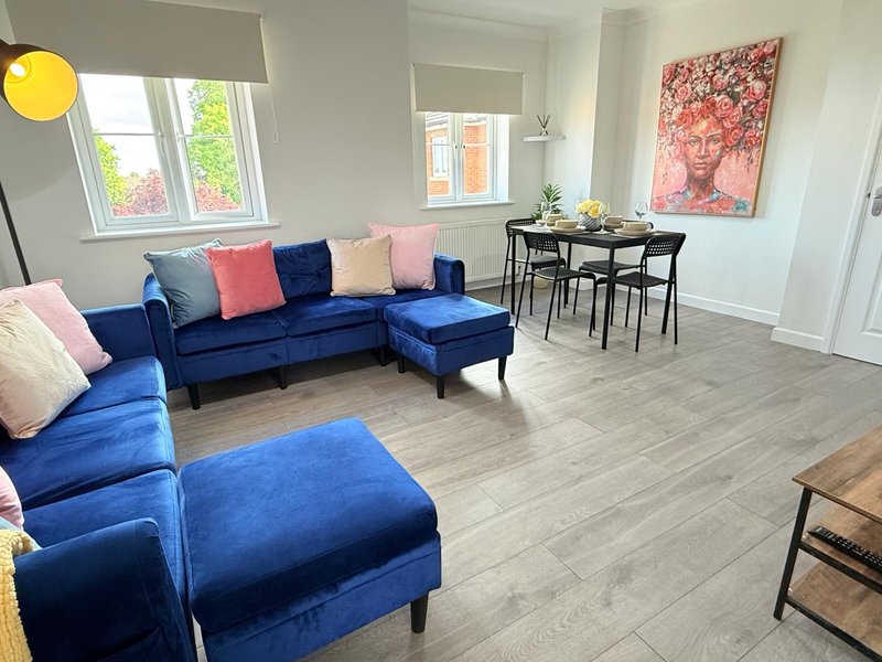Open-plan living room with blue corner sofa, cushions, dining table and chairs, artwork on wall