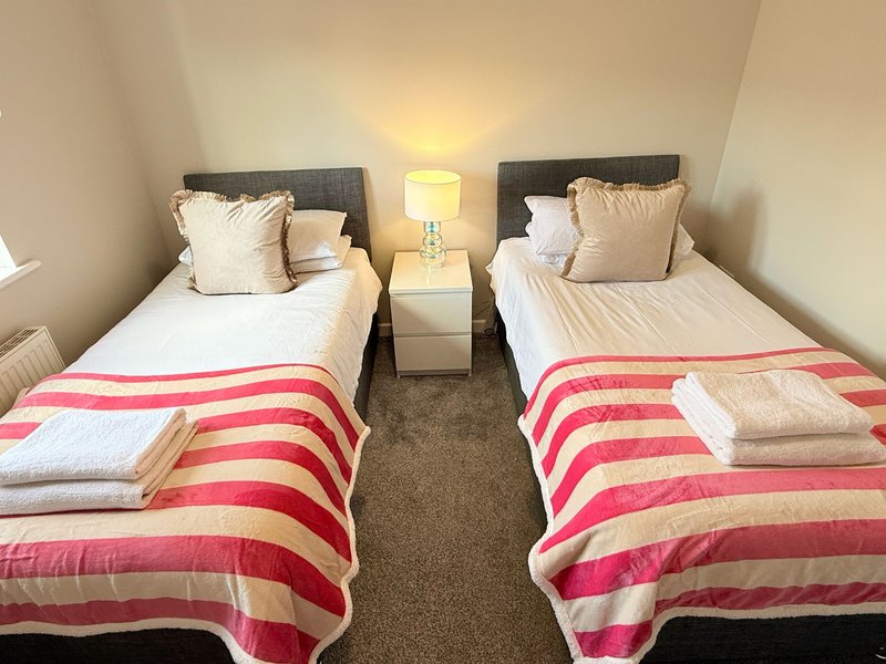 Twin bedroom with two single beds, striped pink and cream blankets, neutral pillows and bedside lamp.