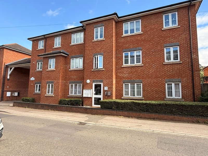 Red brick apartment building with multiple windows, driveway and front entrance