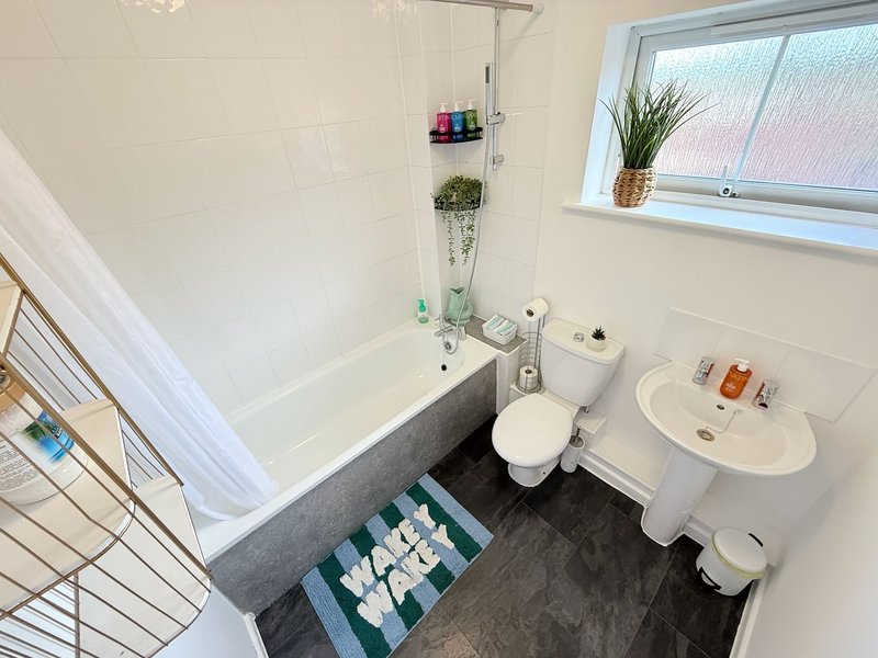 Modern bathroom with bathtub, toilet, pedestal sink, window and towel storage