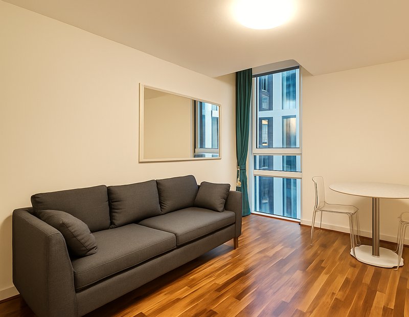 Modern living room with dark grey sofa, wooden floor, mirror and windows with curtains