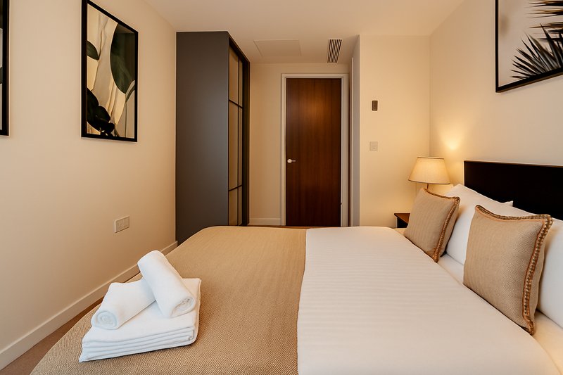 Modern bedroom with double bed, white pillows, rolled towels, lamp and wall art