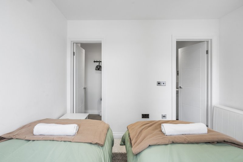 Twin bedroom with two beds, white pillows, beige throws, and ensuite doors