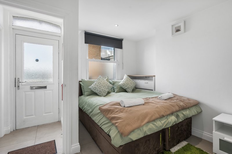 Bedroom with double bed, green bedding, brown throw, decorative pillows and door to hallway