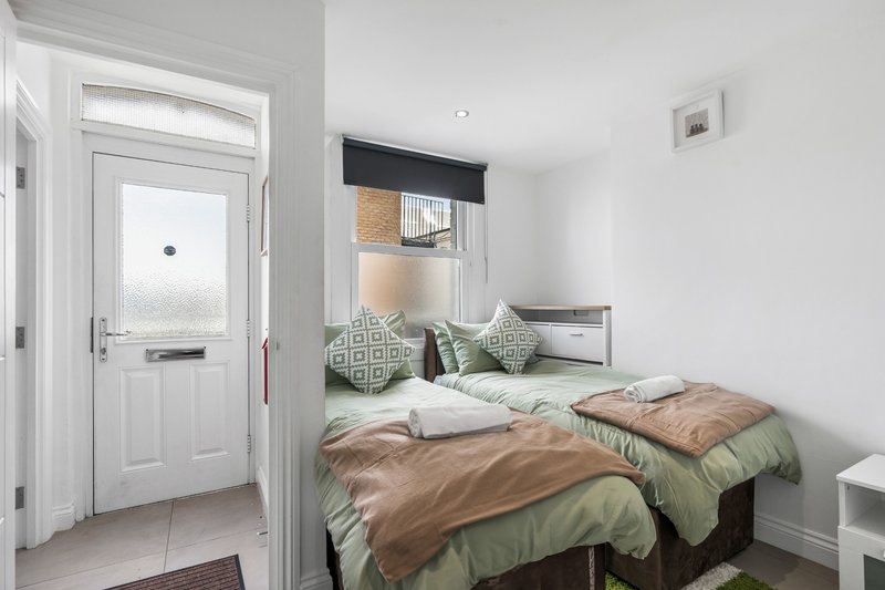 Bedroom with double bed, green bedding, brown throw, geometric cushions and entrance door