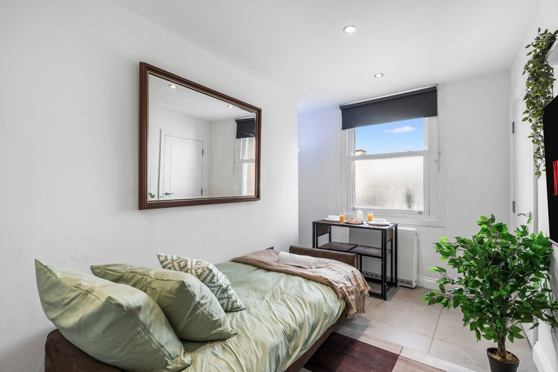 Bright bedroom with double bed, wall mirror, desk by window, and potted plants