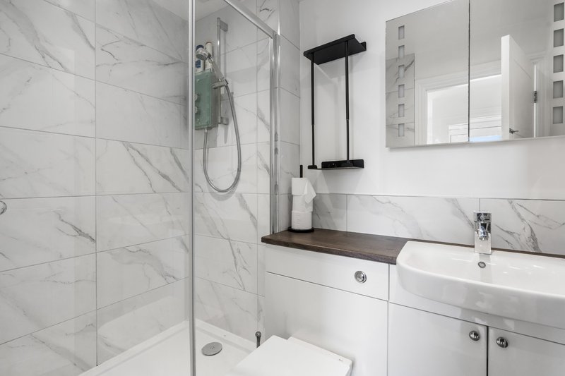 Modern bathroom with marble tiles, glass shower enclosure, white vanity and mirror