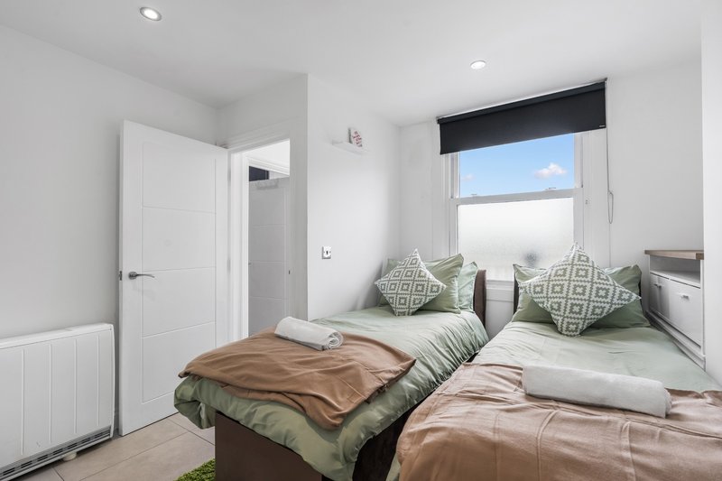 Bright bedroom with two single beds, green bedding, patterned cushions and large window with natural light