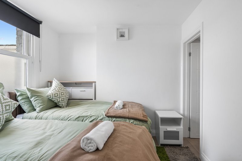 Bright bedroom with twin beds, green bedding, pillows, white walls and window