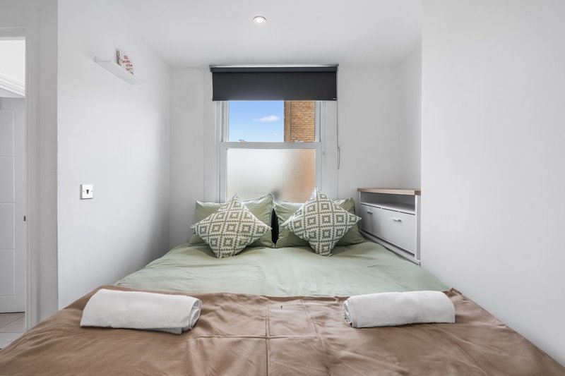 Small bedroom with double bed, patterned cushions, window with blind, and wooden floor
