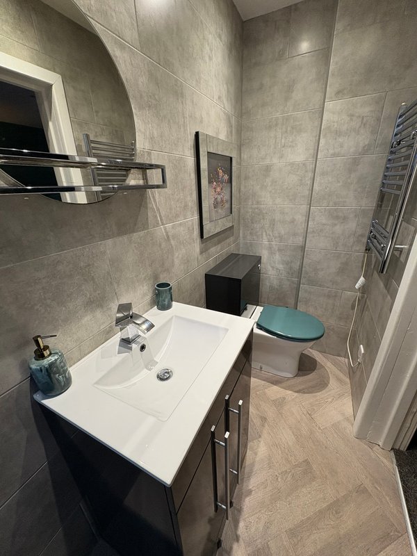 Modern bathroom with white sink, gray tile walls, toilet, and heated towel rack
