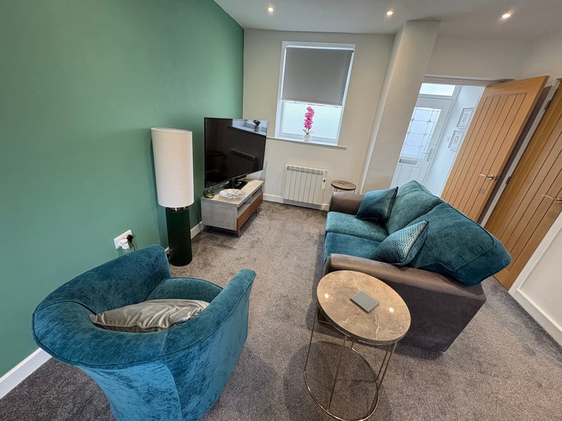 Modern living room with turquoise armchairs, TV, side table, and mint green accent wall