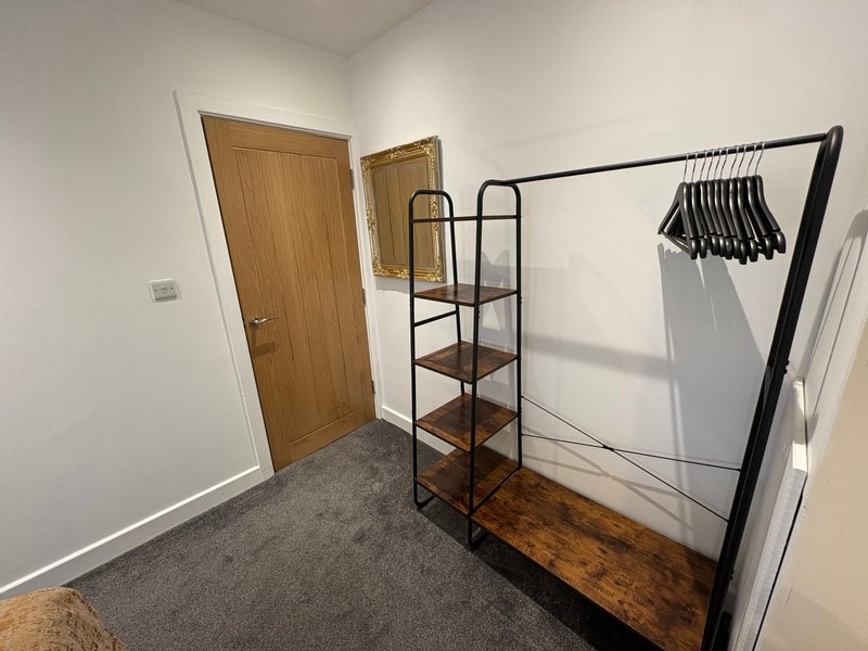 Bedroom with wooden door, shelving unit, clothing rack with hangers, and grey carpet flooring