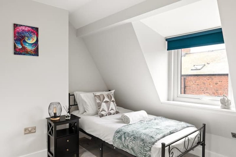 Bright attic bedroom with single bed, black bedside table, framed artwork and angled ceiling