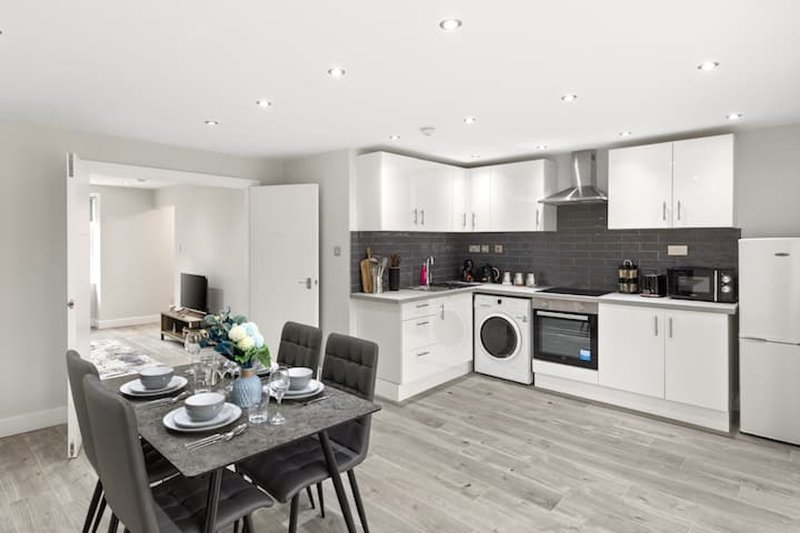 Modern open-plan kitchen and dining area with white cabinetry, black backsplash, and dining table