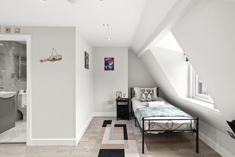 Bright attic bedroom with single metal bed, skylight window, wooden floor and en-suite bathroom