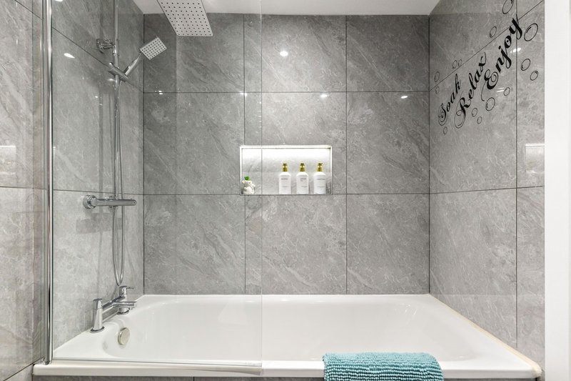Modern bathroom with walk-in shower, gray tile walls, white bathtub and turquoise towel