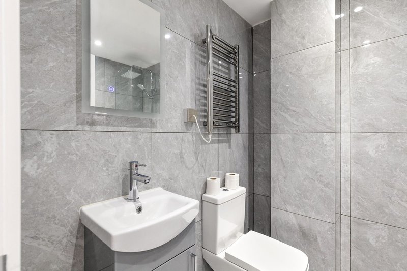 Modern bathroom with gray tile walls, white sink, toilet, mirror and towel rail
