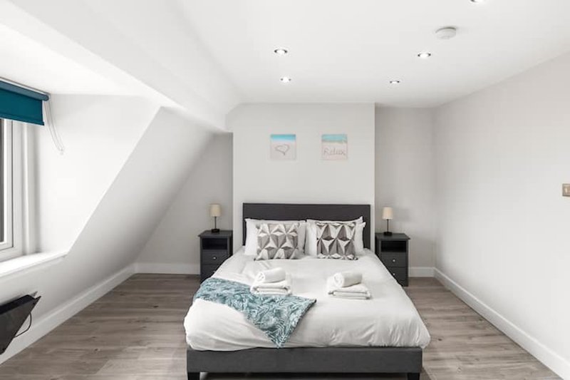 Modern attic bedroom with double bed, dark headboard, patterned pillows and white bedding