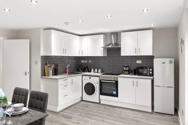 Modern white kitchen with dark splashback, built-in appliances and dining table