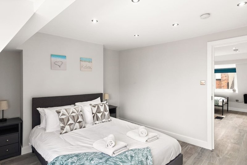 Modern bedroom with double bed, geometric patterned pillows, white bedding, and open doorway to en-suite