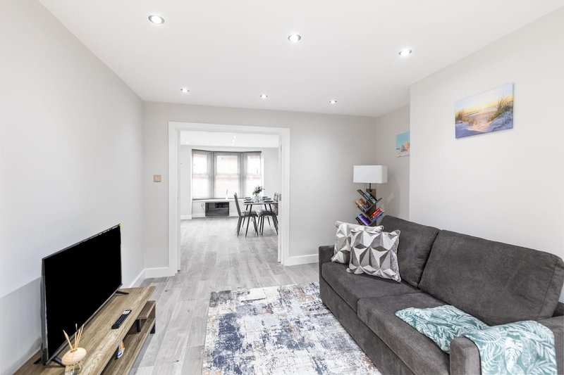 Open-plan living room with gray sofa, TV, dining area visible through doorway