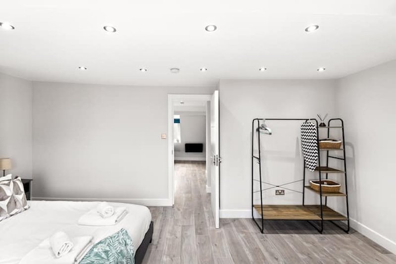 Modern bedroom with white bed, wooden floor, metal clothing rack and ensuite door