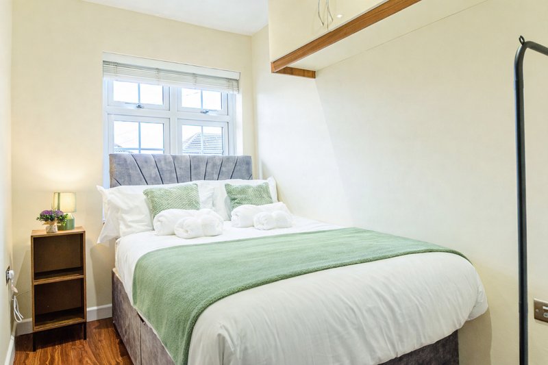 Bright bedroom with double bed, green throw, white bedding, wooden nightstand and window
