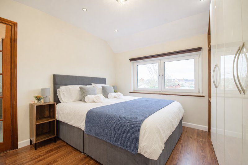Bright bedroom with double bed, blue throw, wooden nightstand and large window
