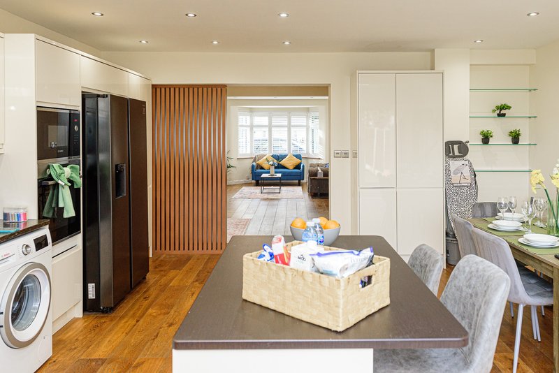 Open-plan kitchen and living area with white cabinetry, wooden flooring, and dining table