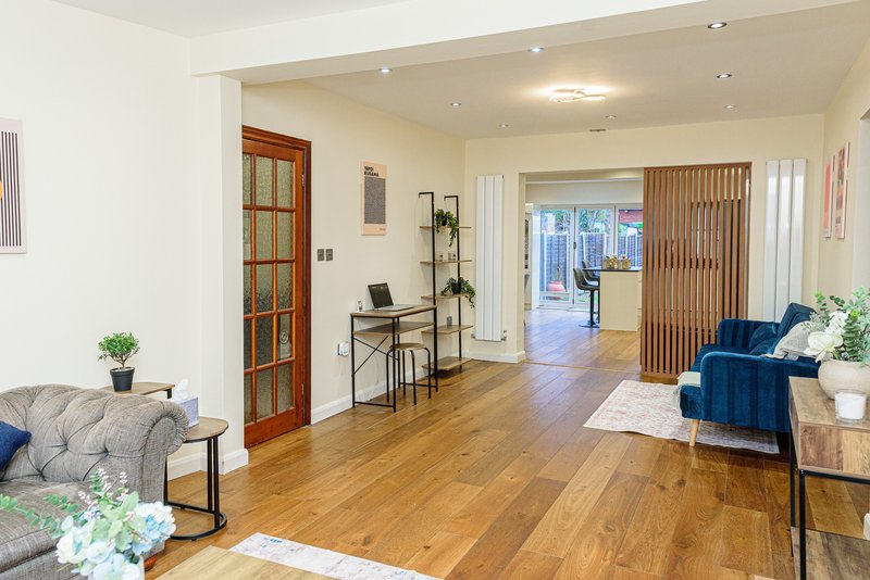 Open-plan living area with wooden flooring, grey sofa, blue armchair, desk and glass doors leading to garden