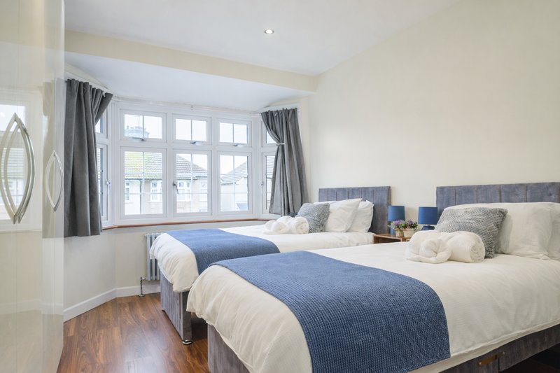 Bright bedroom with two twin beds, blue throws, wooden floor and large windows