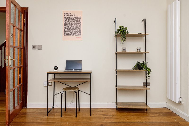Home office with desk, laptop, wooden chair, wall shelving with plants and decor