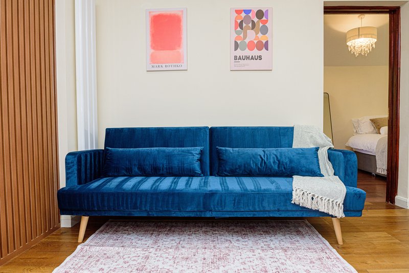 Modern living room with blue velvet sofa, wooden floor, and abstract wall art