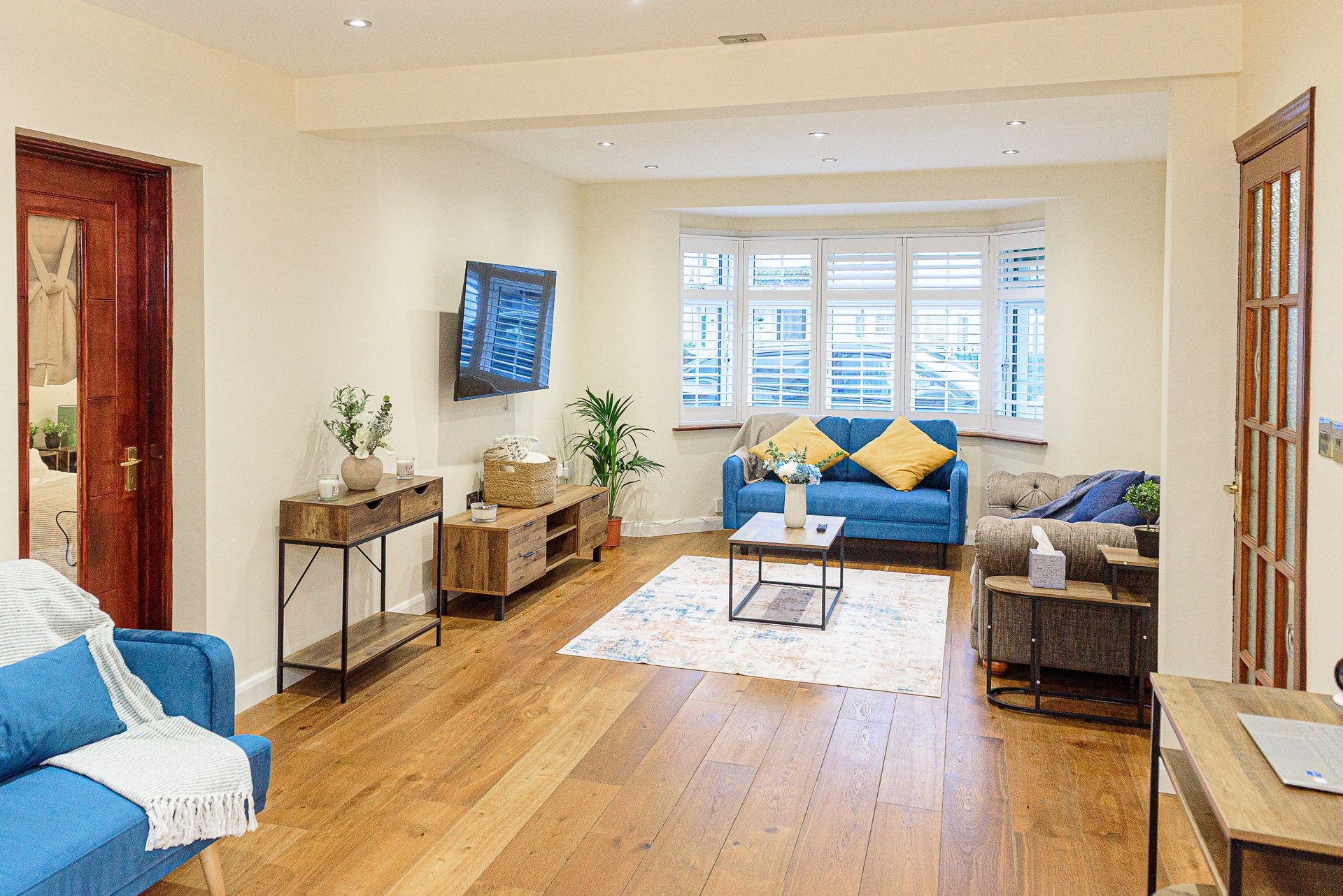 Bright living room with blue sofas, wooden floor, shuttered windows and modern furnishings