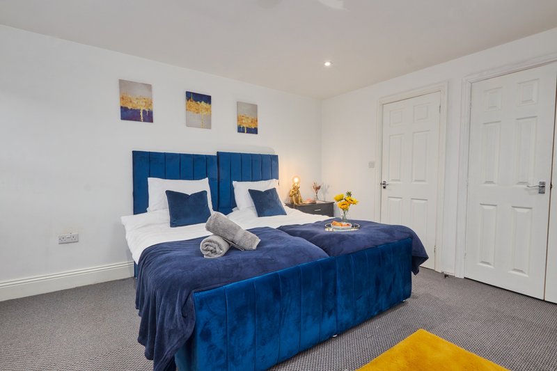 Bright bedroom with two single beds, blue upholstered headboards, white doors and neutral carpet.