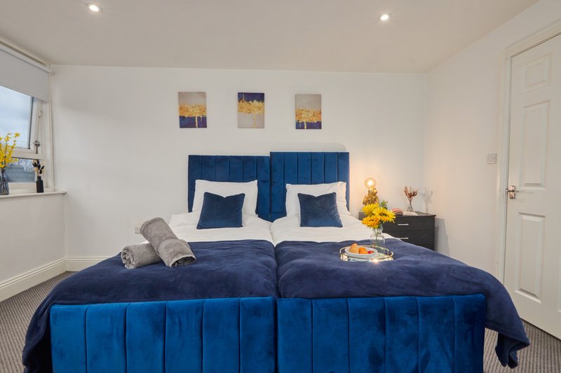 Modern bedroom with blue velvet bed, white pillows, bedside tables, and wall art