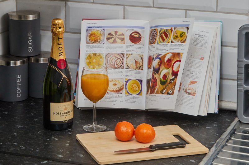 Modern kitchen counter with champagne bottle, juice glass, cookbook, fresh oranges and branded appliances