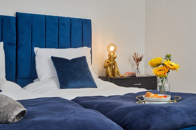 Modern bedroom with blue velvet headboard, white and navy bedding, gold lamp and yellow flowers