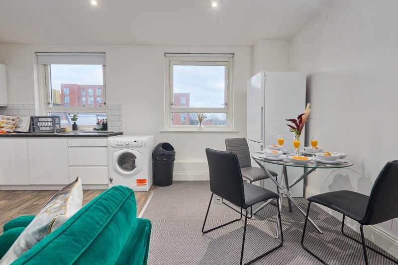 Open-plan studio with kitchenette, dining table, teal sofa and city views from windows