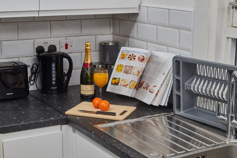 Modern kitchen counter with kettle, champagne bottle, orange juice, fresh fruit, and cooking utensils
