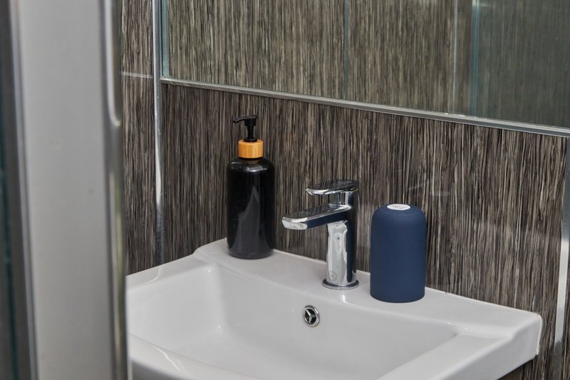 Modern bathroom sink with chrome tap, soap dispenser and toiletries on countertop