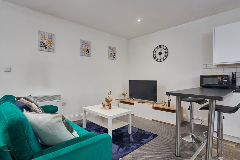 Open-plan living area with turquoise sofa, TV, kitchenette, and wall art