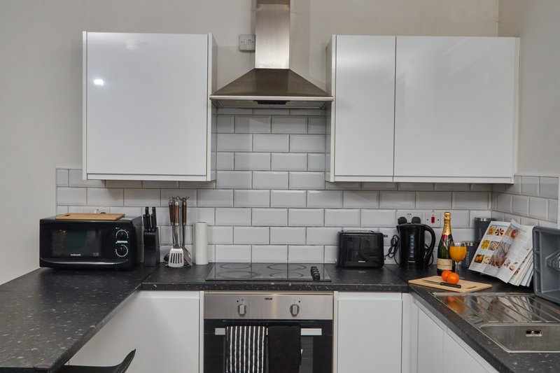 Modern kitchen with white cabinets, black countertop, subway tile backsplash and stainless steel hood