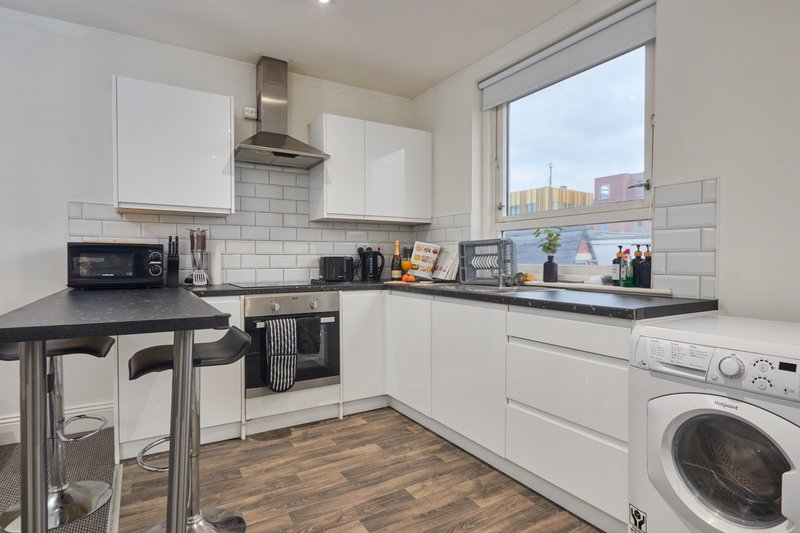 Modern white kitchen with black countertops, subway tile backsplash, washing machine and dining table
