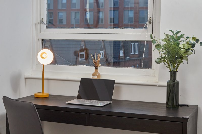 Modern desk workspace with laptop, yellow lamp, flowers, and city view through window