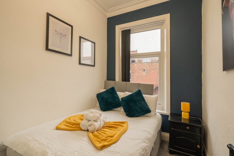 Compact bedroom with single bed, yellow bedding, dark teal cushions and small black bedside table