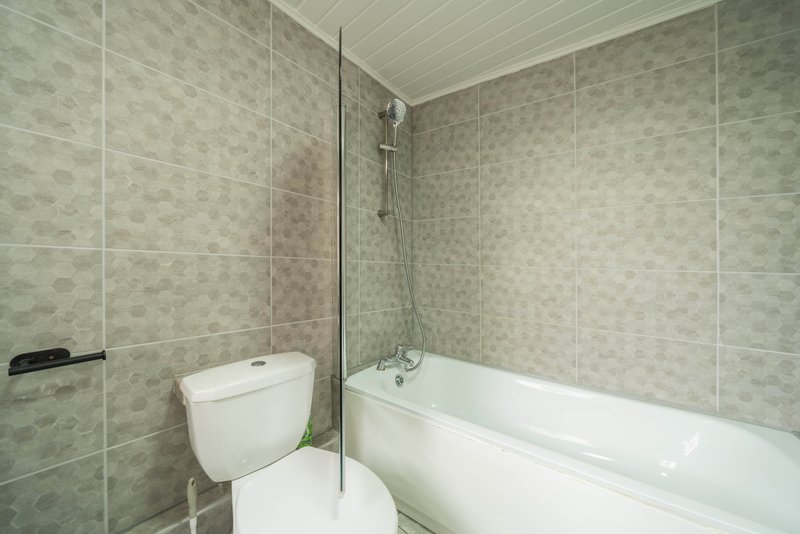 Modern bathroom with white toilet, bathtub, glass shower enclosure and tiled walls