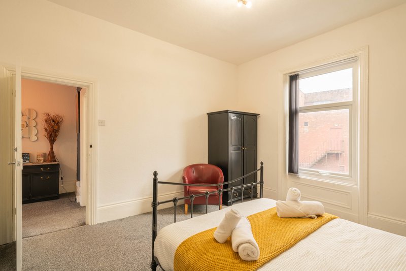 Bright bedroom with double bed, yellow throw, metal frame, and adjoining room visible through doorway