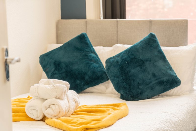 Bedroom with double bed, teal cushions, white pillows and yellow throw blanket